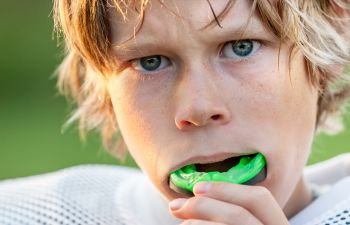 A boy in a rugby sports kit putting in his mouth guard before coming back to play.