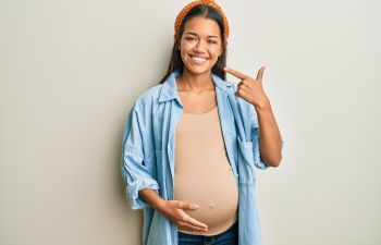 Pregnant woman with a perfect smile pointing at her teeth.